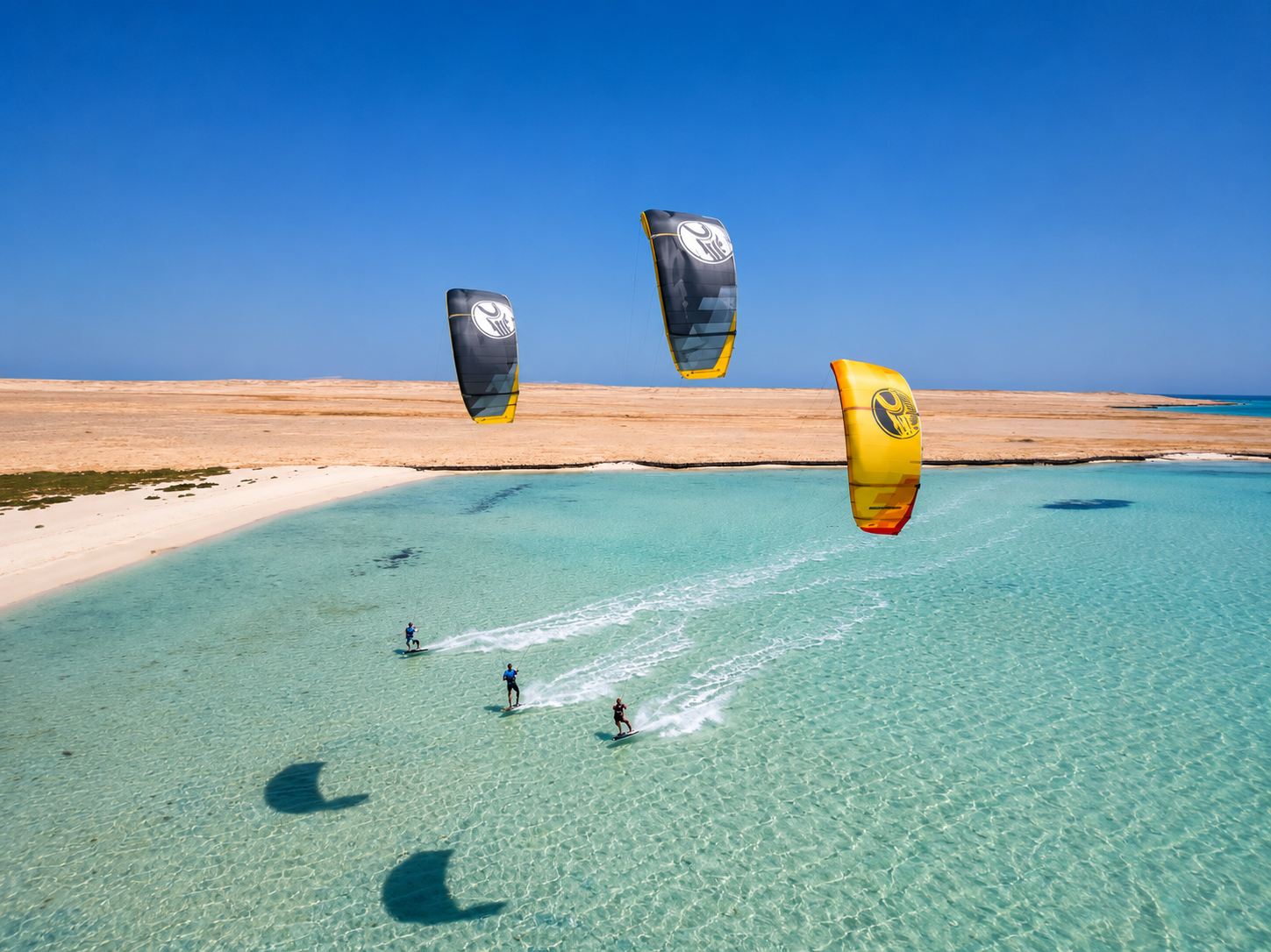 Three kitesurfers gliding across a crystal-clear shallow lagoon