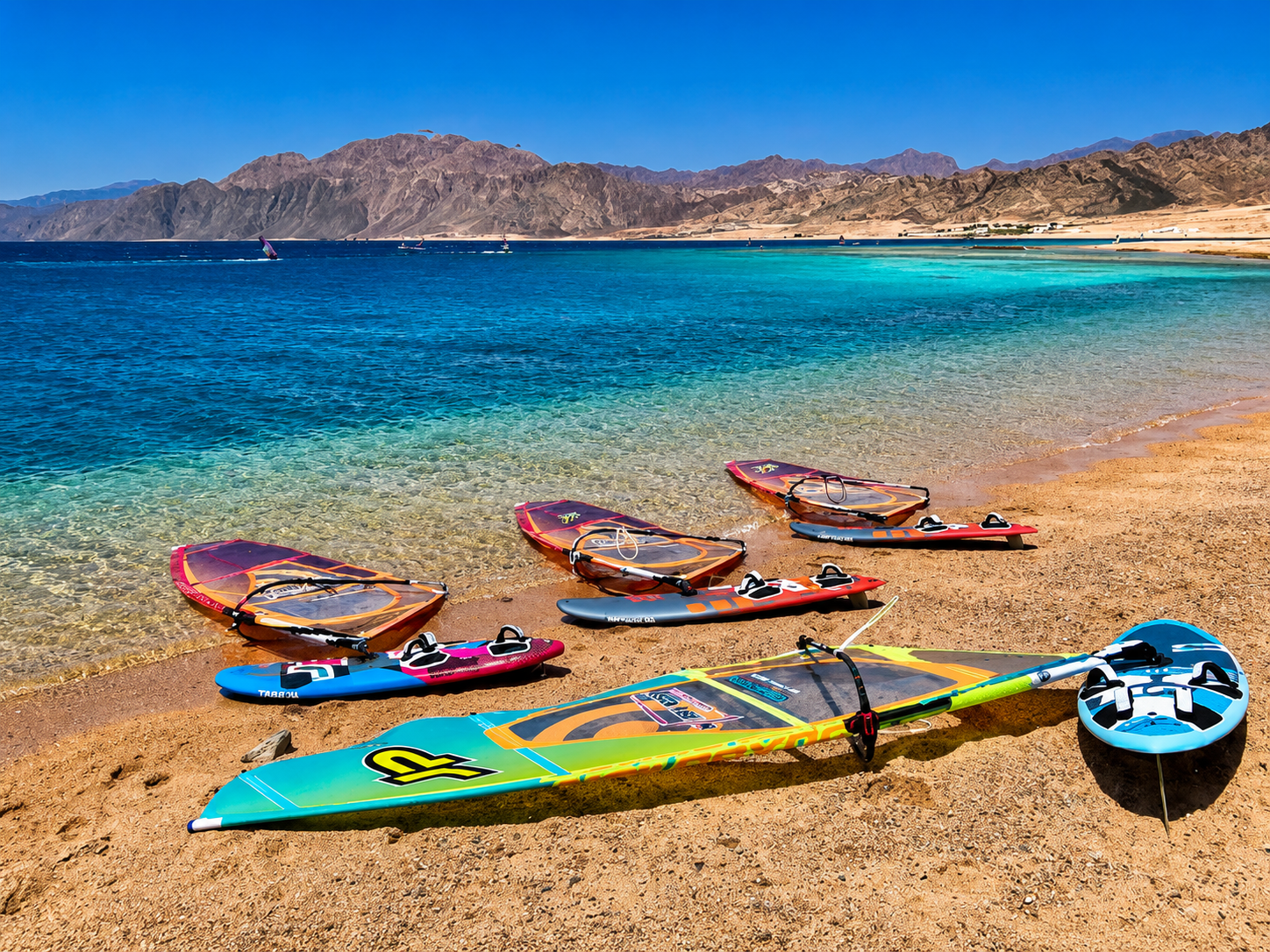 Windsurfing boards and sails ready on the Red Sea shoreline below desert mountains